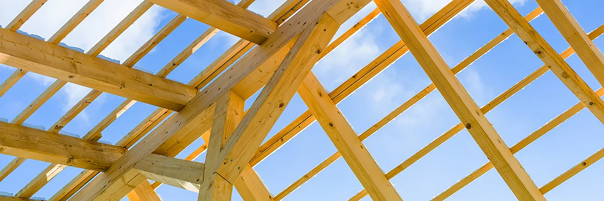 Konstrukcja więźby dachowej widziana od środka, krokwie i łaty na tle błękitnego nieba