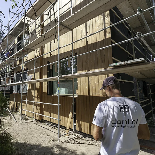 Monter w koszulce z logo Dombal przed elewacją drewnianą montowaną na rusztowaniu