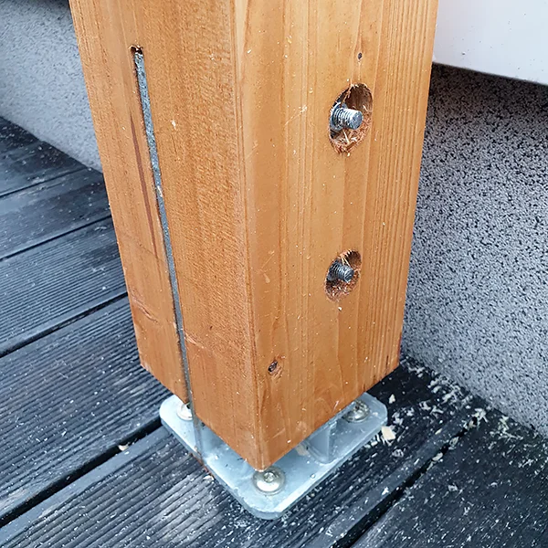 Dolny odcinek drewnianego słupa osadzonego na stalowej płycie przykręconej do tarasu, w boku słupa wpuszczone śruby